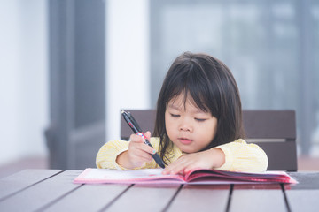 Cute little girl doing homework, reading a book, coloring pages, writing and painting. Children paint. Kids draw. Preschooler with books at home. Preschoolers learn to write and read. Creative toddler