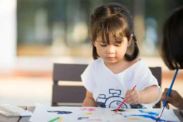 little asian girl painting with paintbrush and colorful paints