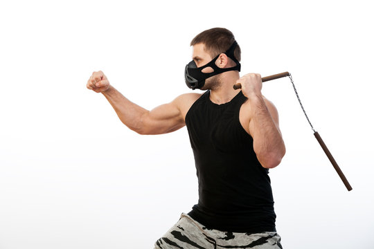 A young athletic man in a sport shirt, a training black mask holds a nunchaks on a white isolated background