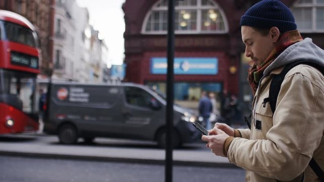 Young man using his phone as he walks on the high street, in slow motion