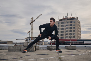one young man stretching outdoors on rooftop. Buildings crane behind, cityscape, urban area.
