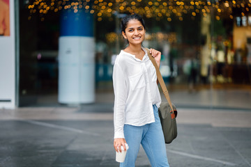 Portrait of young, attractive Indian woman holding a green sling bag and coffee cup in the day and...