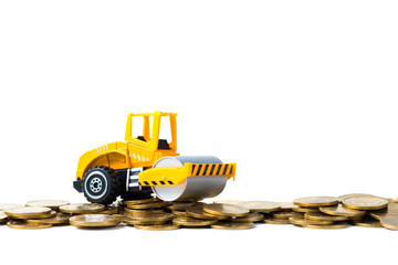 Mini Road roller machine with pile of gold coin, isolated on white background with copy space, business finance and banking industrial concept.