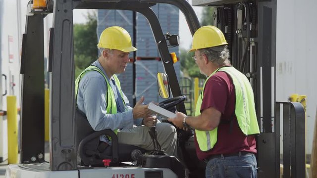 Truck driver and forklift driver talk at shipping facility.  Fully released for commercial use.