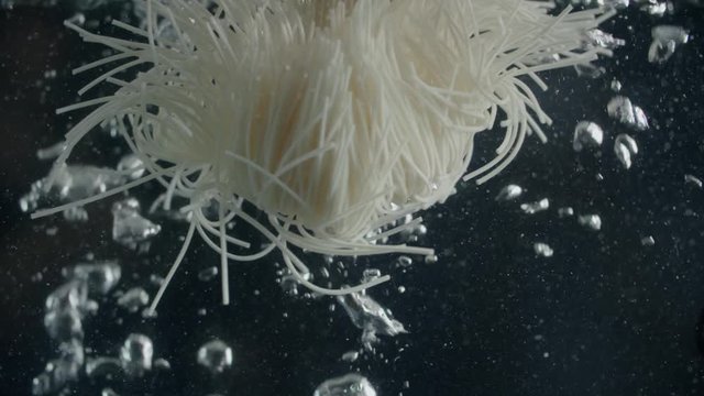 cooking noodles, raw spaghetti drops into boiling water slow motion black background