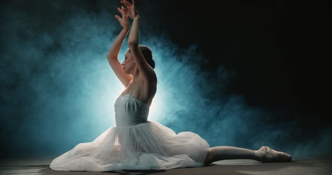 Ballerina performs elements of classical ballet in the studio, black background, smoke, slow motion