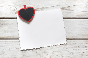 Valentine's card. Red clothespin as heart and sheet for your text on wooden board. Copy space. View from above.