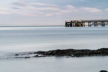 Looking across the Bay to Fishermen on Cornwallis Wharf on a Summer Evening in Auckland New Zealand - Long Exposure