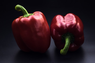 Two red peppers on black background