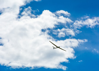 A Glider flying in bleu sky with big white clouds. The glider is a plane that has no engine