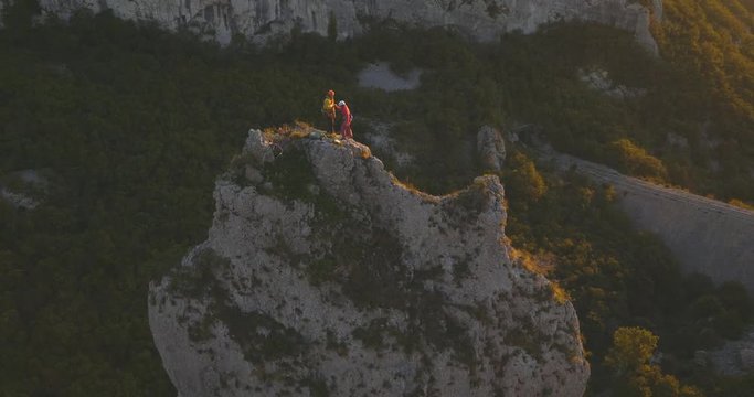 Aerial circling around friends rock climbing reaching the top and celebrating together at sunset.
