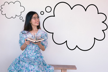 A cute Asian Woman Wearing Vintage blue dress sitting and reading on the bench, thinking with...