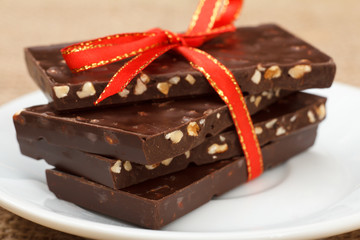 Chocolate bars with nuts tied with red ribbon on white saucer