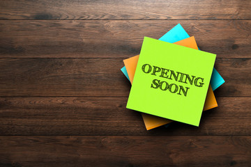 Opening Soon, the phrase is written on multi-colored stickers, on a brown wooden background. Business concept, strategy, plan, planning.