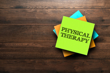 Physical Therapy, the phrase is written on multi-colored stickers, on a brown wooden background. medical concept