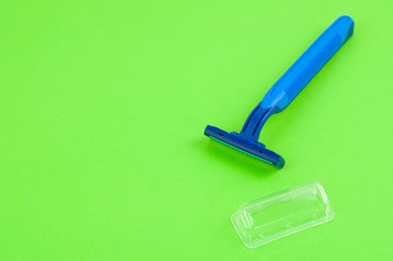 Single new blue plastic disposable razor with two blades and humid strip near transparent cover on blank green paper