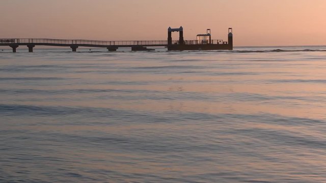 seebr&uuml;cke zum sonnenaufgang bei windstille mit leichtem Wellengang in Warmes Licht getaucht