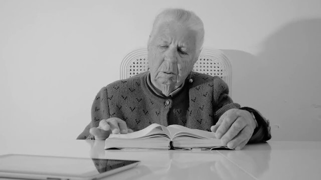Close-up of a woman eighty-three years old slowly turn the pages of the book, sitting at the table at home.