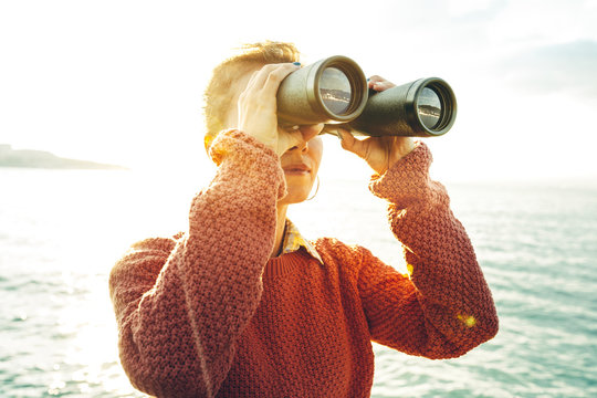 Beautiful Young Girl Looking Through Binoculars At The Sea On A Bright Sunny Day. Wanderlust Journey Concept