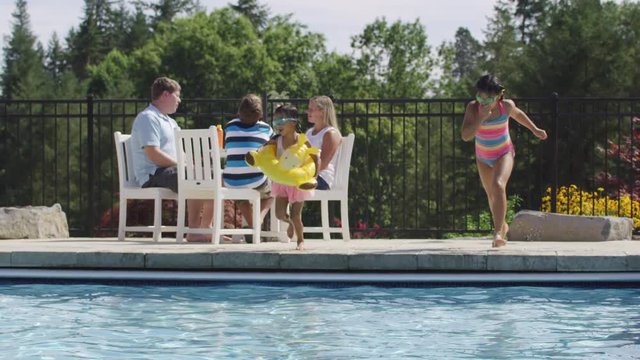 Girls jumping into backyard pool in slow motion