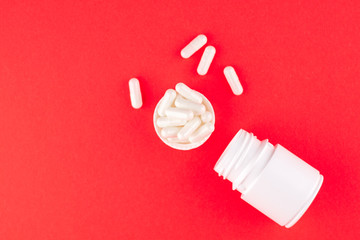 Close up white pill bottle with spilled out pills and capsules in cap on scarlet red background...