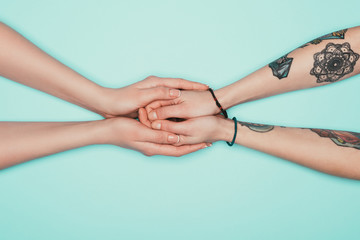 cropped shot of sensual women holding hands of each other isolated on turquoise