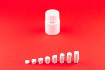 Close up pyramid concept of white pills and bottle on scarlet red background with copy space. Focus on foreground, soft bokeh. Pharmacy drugstore concept