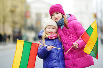Two adorable little sisters celebrating Lithuanian Independence Day holding tricolor Lithuanian flags