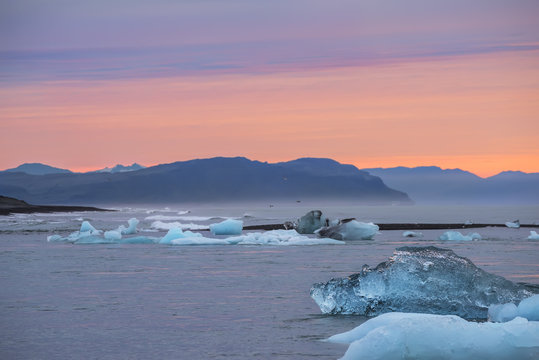 The coast of the Atlantic Ocean. Glacial lagoon. the ice floes are floating on the water and the silhouettes of the mountains in the haze at dawn. Beautiful northern landscape
