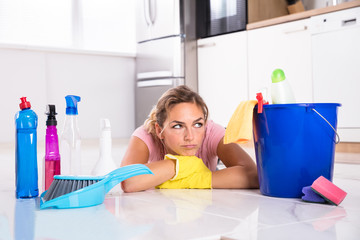 Woman Lying On Kitchen Floor And Looking At Cleaning Products