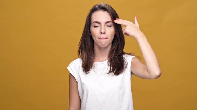 Young displeased woman standing isolated over yellow background while looking camera make gun gesture near head