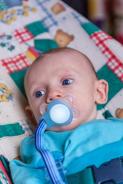 Infant boy with a pacifier lying down and looking to the side.