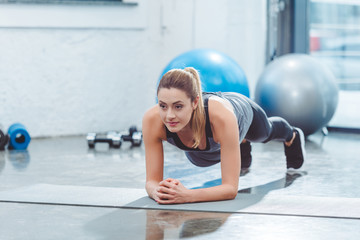 sporty young woman doing plank exercise on yoga mat