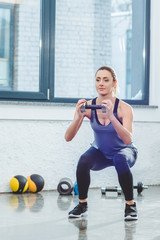 athletic young woman doing squat exercise and holding dumbbell in gym