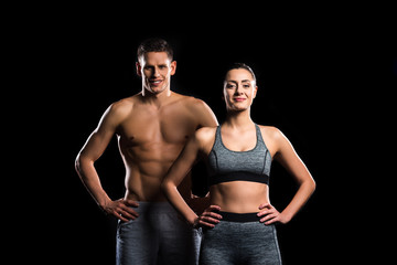 Fototapeta na wymiar sporty young couple standing together and smiling at camera isolated on black