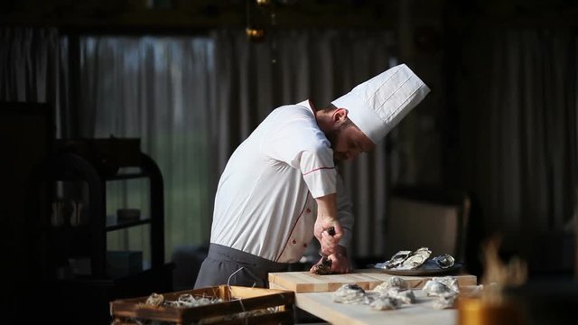 Chef in a luxury restaurant opens oysters and puts them on a plate with ice