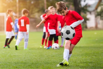 Tuinposter Boy kicking football on the sports field © Dusan Kostic