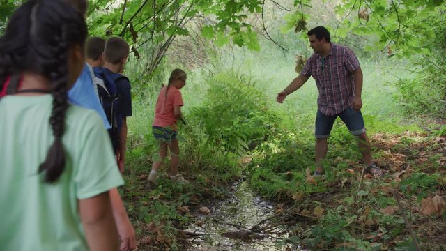 Kids at summer camp cross small creek on nature walk