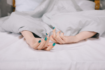 cropped image of girl with manicure lying under blanket on bed