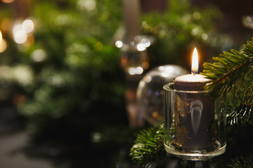 Christmas decorated table with green branches of spruce, balls and burning candle in cozy restaurant.