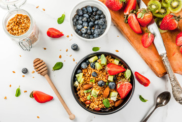 Healthy breakfast with muesli or granola with nuts and fresh berries and fruits - strawberry, blueberry, kiwi, on white table, copy space