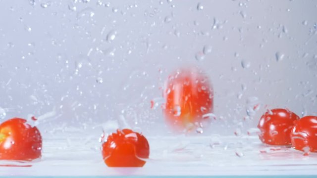 Tasty fresh wet red tomatoes falling in water with big splashing. Slow motion.