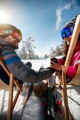 Couple spending time together and drink after skiing in ski resort. Back view - obrazy, fototapety, plakaty