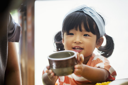 Close up of young girl with black pigtails and blue hairband holding a ceramic bowl.