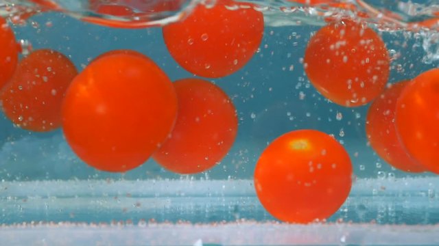 Tomatoes fall in blue fresh water. High speed camera shot.