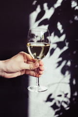 White wine in a glass in hand, rustic background, selective focus. Shadows on the wall.