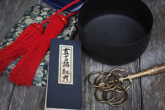 High angle close up of Buddhist prayer text, red silk tassel of a mala and black singing bowl.