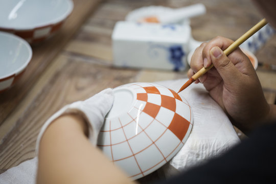 Close up of person working in a Japanese porcelain workshop, painting geometric pattern onto white bowls with paintbrush.