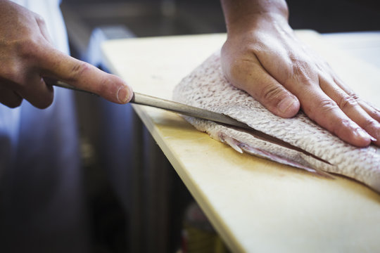 High angle close up of chef working at a counter at a Japanese sushi restaurant, slicing fillet of fish.