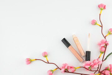 Obraz na płótnie Canvas Nude pink lip gloss decorated with fake pink flower branches on white background with copy space